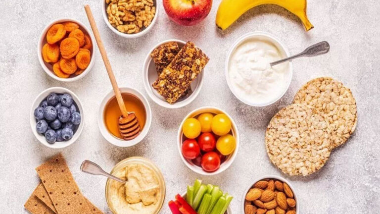 Imagem de alimentos saudáveis como amêndoas, iogurte e abacate, mostrando opções nutritivas para lanches entre as refeições."