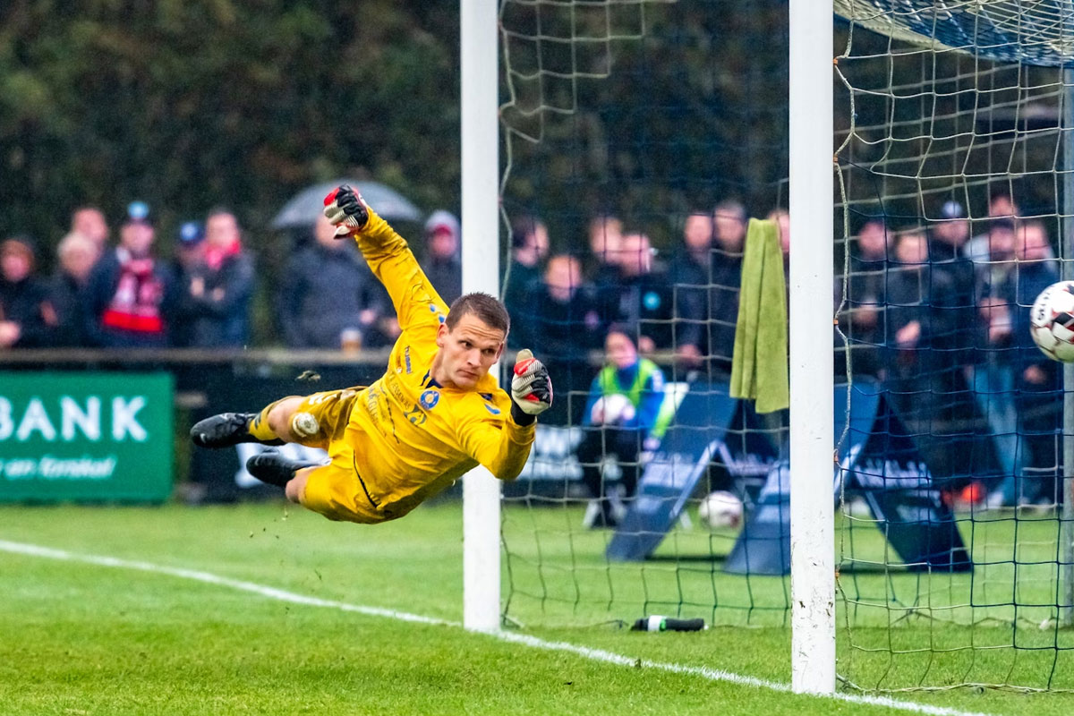 "Goleiro em pleno salto estendido, tentando defender a bola antes que entre no gol."