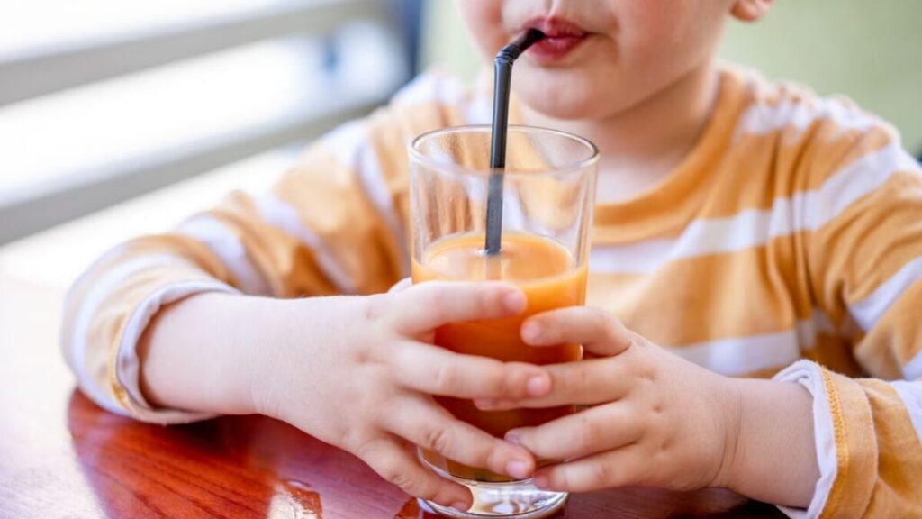 Criança bebendo suco de cenoura com canudo em copo de vidro